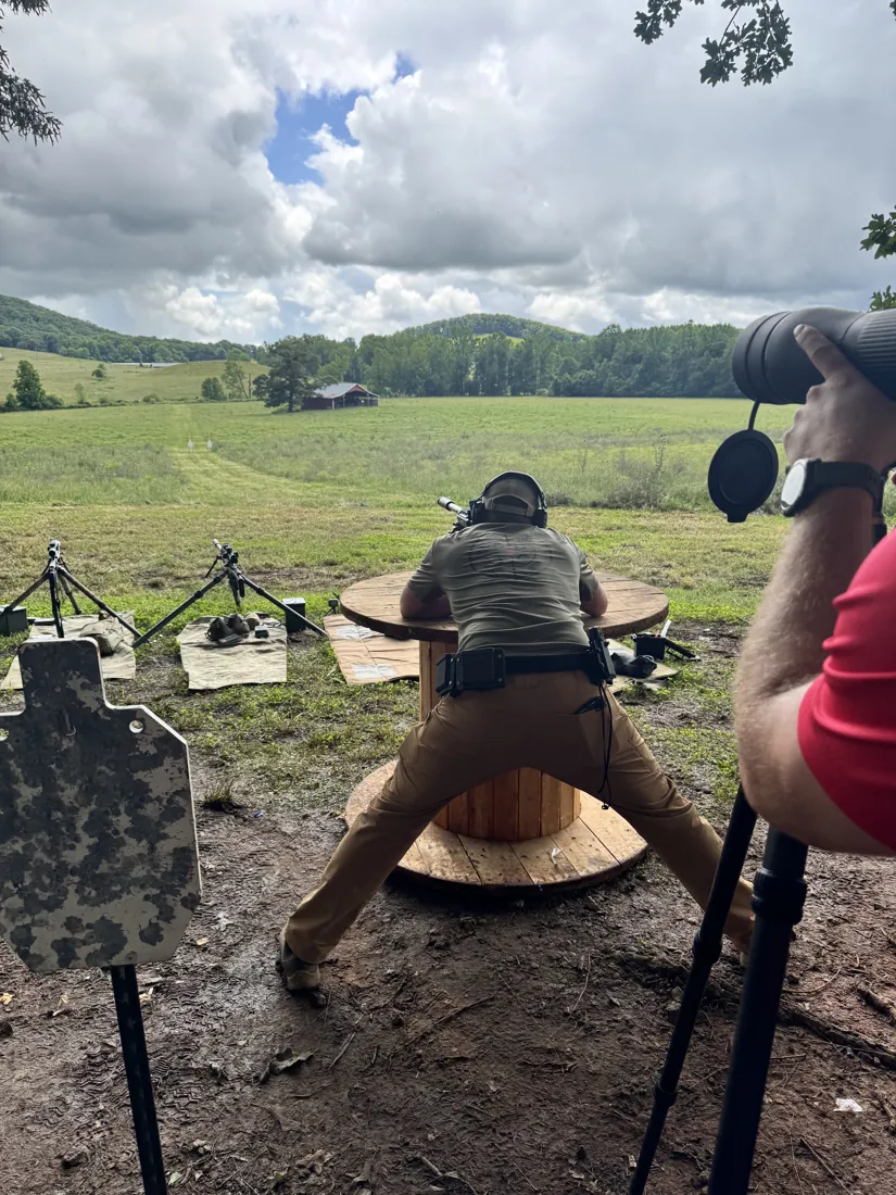 A precision shooter and spotter at a bench rest with mountains behind the range