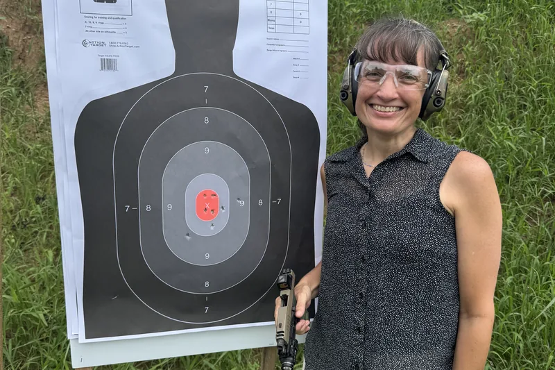 A woman smiling at the range after firing a tight shot grouping into the target during a Ladies Pistol class